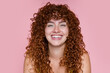 © mahalo studio/Stocksy - redhead woman with curly hair smiling on pink background