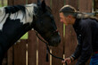 © Connect Images - Person with long hair gently interacting with a black and white horse near a wooden fence. Brandenburg, Germany