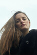 © Connect Images - Woman with long brown hair and black coat looking down against a clear sky. Berlin, Germany