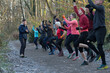 © Connect Images - A group of diverse people dressed in athletic clothing exercises energetically on a wooded trail, guided by an instructor. Sale Water Park, Manchester, UK