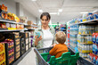 © Santi Nuñez/Stocksy - Mother using smartphone while shopping with child in supermarket cart