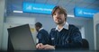 © Framestock - Airport Security Check: Portrait of TSA Worker Using Laptop, Looking at Camera. Transportation Security Administration for Travel Safety. In Background, Airport Staff Conducting Screening Procedures.