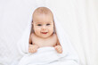 © Any Grant - cute little newborn baby with blue eyes on the bed in a white towel after bathing or washing, happy baby at home on a cotton bed smiling