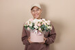 © New Africa - Smiling delivery man holding gift box with beautiful floral composition on beige background
