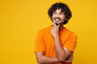 © ViDi Studio - Young smiling happy Indian man he wear orange t-shirt casual clothes put hand prop up on chin, lost in thought and conjectures isolated on plain yellow background studio portrait. Lifestyle concept.