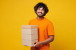 © ViDi Studio - Young smiling fun happy Indian man he wear orange t-shirt casual clothes hold stack cardboard blank boxes look camera isolated on plain yellow background studio portrait. Lifestyle, service concept.