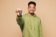 © ViDi Studio - Young man of African American ethnicity in green hoodie casual clothes hold car key fob keyless system stretch hand to camera isolated on plain pastel light beige background studio Lifestyle concept