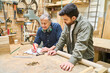 © Robert Kneschke - Experienced artisan instructs young apprentice in lumberyard teamwork