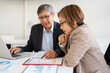 © Fahng - Asian senior businesswoman and man working in office. Mature employee colleagues sitting on table considering paper document graph , using laptop computer device plan project in corporate workplace.