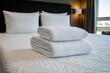 © Nataliya - Freshly folded white towels on a neatly made hotel bed