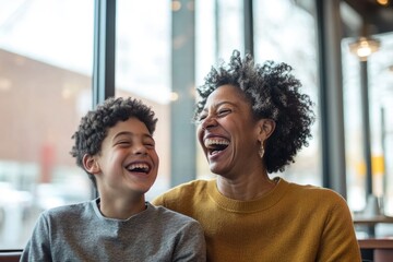 Wall Mural - cheerful image of mother and her teenage son laughing together at coffee shop natural light pouring 