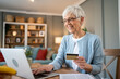 © Migma_Agency - Happy senior woman using laptop and credit card for online shopping at home