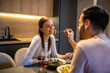 © Mediteraneo - Couple dining together in their apartment. They drink wine and feed each other.