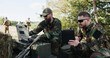 © ABCreative - Soldiers in camouflage uniforms, equipped with helmets and backpacks, analyze battle strategy at the training ground, entering data into a system and discussing tactics while holding a tablet.