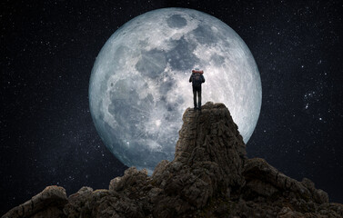 Wall Mural - photomontage of man on top of a mountain observing the full moon