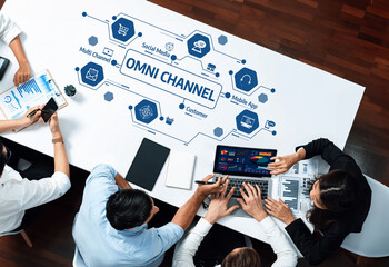 Aufkleber - A diverse group of professionals collaborates around a modern office table, focusing on omni channel strategy with laptops and digital devices, showcasing teamwork and innovation. Amity