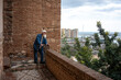 © sutulastock - A senior man in a denim jacket leaning on a railing, overlooking the harbor and city skyline, with a scenic view of the coastline and palm trees