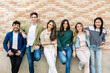 © Xavier Lorenzo - Six young students are posing together leaning against a brick wall, smiling and looking cheerful. Youth community and friendship concept