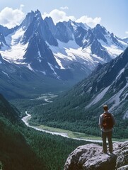 Leinwandbilder - Majestic mountain range under clear skies with a hiker enjoying the breathtaking view of snow-capped peaks and lush valley below