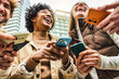 © Davide Angelini - Happy young people using smart mobile phone device outside - Technology concept with guys and girls watching cellphone in city street