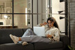 © Pixel-Shot - Female African-American programmer working with laptop on sofa in office at night