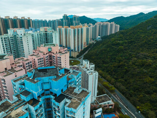 Poster - Aerial panorama of Hong Kong city showcases dense buildings nestled amidst green mountains. Urban landscape view from above.