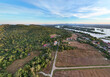 © AmazingAerialAgency - Aerial view of serene rural landscape with river, fields, and forest under a sunny sky, Khong District, Champasak, Laos.