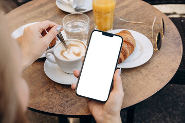 mockup woman's hand holding using smart phone with white blank screen pov at coffee shop, mobile app