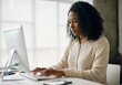 © Running opossum - Young african american businesswoman concentrating while typing on a desktop computer keyboard in a bright, contemporary office space