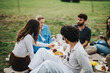 © qunica.com - A group of diverse friends enjoy a relaxing picnic outdoors, surrounded by greenery on a cloudy day, fostering connection and fun.