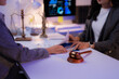 © Tj - Two lawyers are examining legal documents and discussing contract details in a modern office, with a gavel and justice scales symbolizing law and order in the background