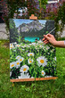 © Tetiana Tuzyk - A colorful painting on an easel in a peaceful outdoor setting, with a brush nearby, capturing the process of creating art in nature.