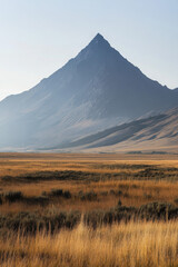 Wall Mural - Tall, solitary mountain peak against a clear sky, with golden grasslands in the foreground capturing the serene beauty of a remote wilderness landscape.