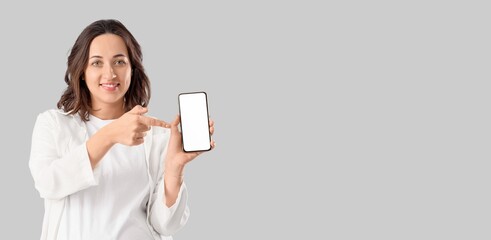 Wall Mural - young pregnant woman pointing at mobile phone on grey background with space for text