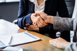 © Phushutter - Two female lawyers in business suits shake hands at wooden desk, finalizing legal agreement. wooden gavel and scales represent justice as they discuss corporate law, compliance, dispute resolution.