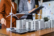 © Phushutter - Two businesswomen sit at a desk in a meeting, discussing property development while building a model of city tower. real estate investments, zoning laws, sustainable energy solutions. net zero