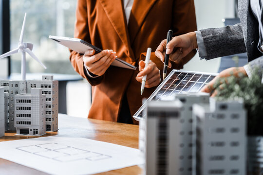 two businesswomen sit at a desk in a meeting, discussing property development while building a model