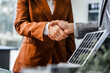 © Phushutter - Two businesswomen shake hands at desk, finalizing deal on property development. real estate investments, zoning laws, sustainable energy solutions while working on city tower model, net-zero goals.