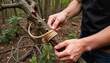 © Elina - Close-up of hands tying rope around a tree branch for securing or crafting in a forest