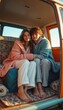 © natakot - A young couple, wrapped in colorful cozy blankets, sits together in a vintage van, radiating warmth and affection. Their bare feet rest on soft blankets, creating an inviting atmosphere of love and