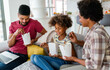 © NDABCREATIVITY - Happy african american family eating on couch with cardboard boxes in living room interior