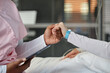 © Seventyfour - Nurse gently holding patient's hand, providing comfort in hospital. Patient wearing medical bracelet, showing caring and compassionate environment
