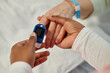 © Seventyfour - Close-up of medical professional using pulse oximeter for monitoring patient's blood oxygen saturation levels, showing hands with device and hospital wristband