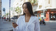 © Krakenimages.com - Young chinese woman using smartphone on urban street in city with white shirt and relaxed expression, standing outdoors