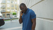 © Krakenimages.com - Young african american man in blue polo shirt talking on mobile phone while standing against a building wall in an urban street setting