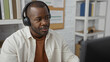 © Krakenimages.com - Young african american man wearing headphones sitting in an office setting with shelves and a corkboard in the background