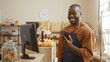 © Krakenimages.com - Young man smiling in a bakery while checking his phone with pastries and bread on shelves in the background