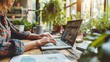 © auttawit - Woman is typing on a laptop in front of a potted plant