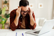 © djile - Businessman suffering from headache while working remotely on laptop at home