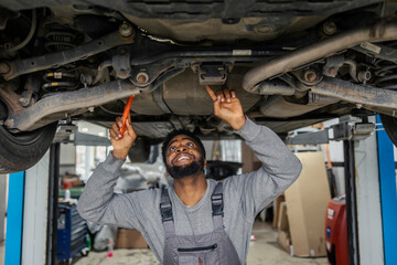 Fototapete - Interracial auto mechanic standing under chassis and looking for malfunction auto repair shop.